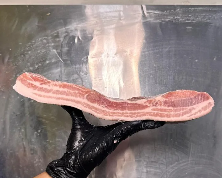 Potongan samcam segar dipegang petugas bersarung tangan di ruang potong Aruna Pork Supply